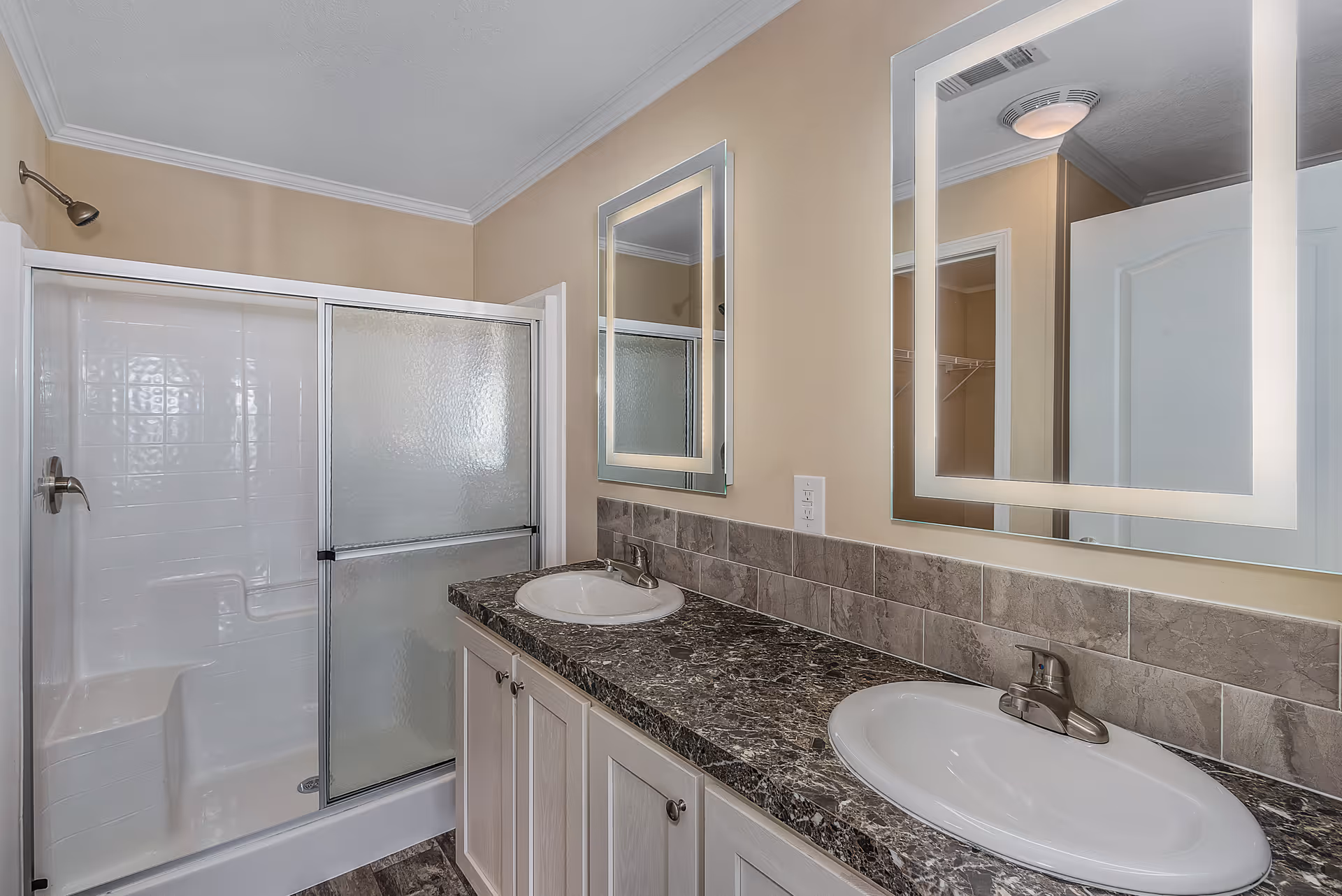 Modern bathroom with a double sink vanity featuring a dark marble countertop, two illuminated rectangular mirrors above the sinks, and a shower with sliding frosted glass doors and a built-in seat.