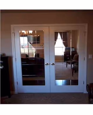 White double French doors open to a living room with chairs and windows.