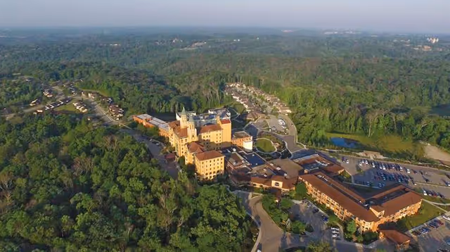 Aerial view of a large multi-building senior living campus surrounded by trees with parking lots and access roads.