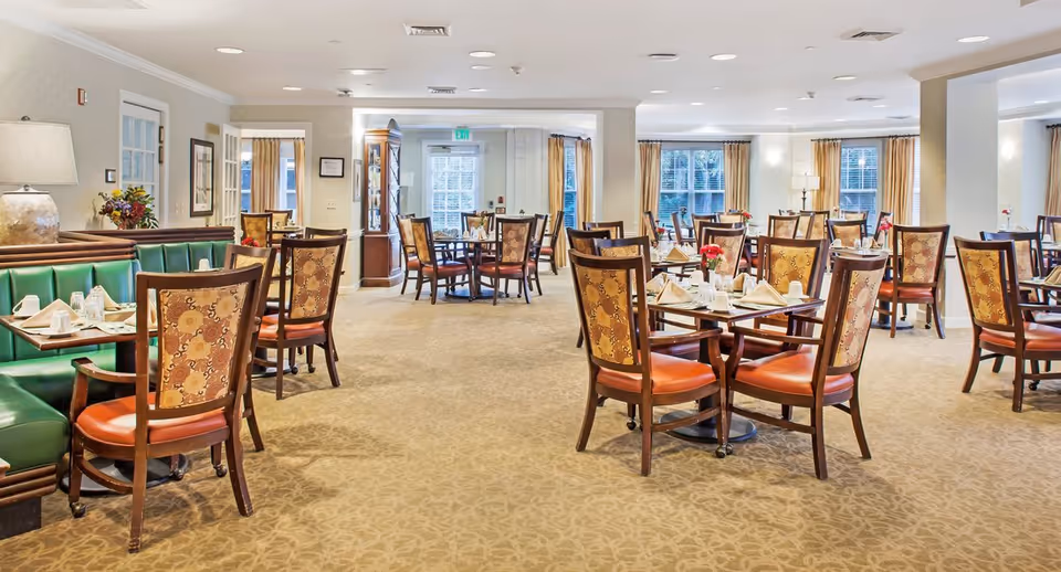Dining room with multiple set tables, upholstered chairs, and booth seating in a bright, well-lit room.