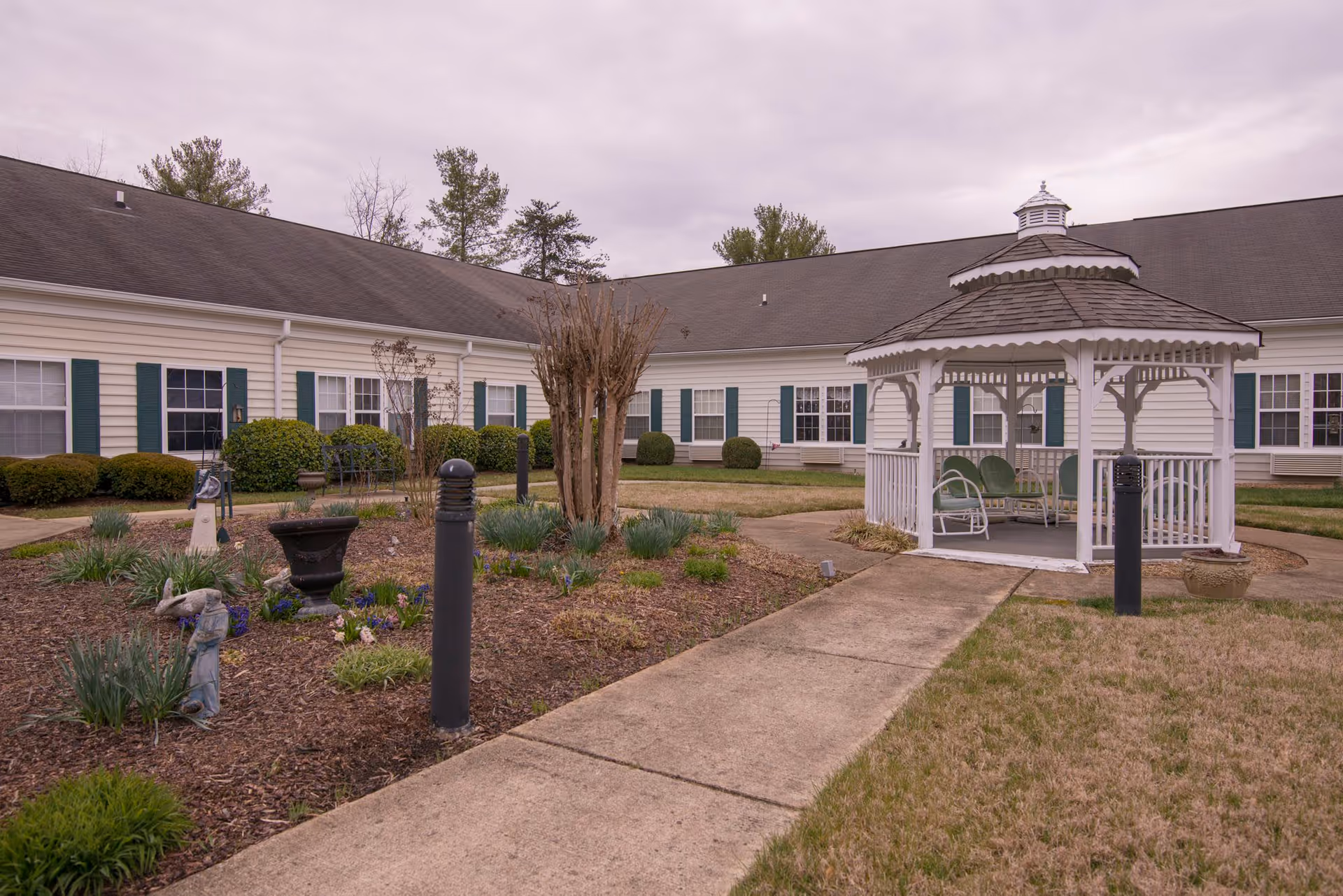 A white gazebo sits in a landscaped courtyard with walkways in front of a single-story senior living building.