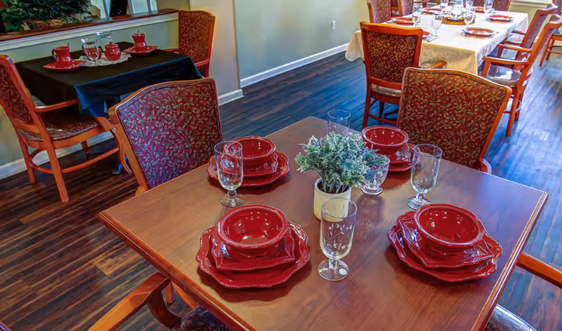 Wooden dining tables set with red plates and bowls, glassware, and a small potted centerpiece in a dining area.