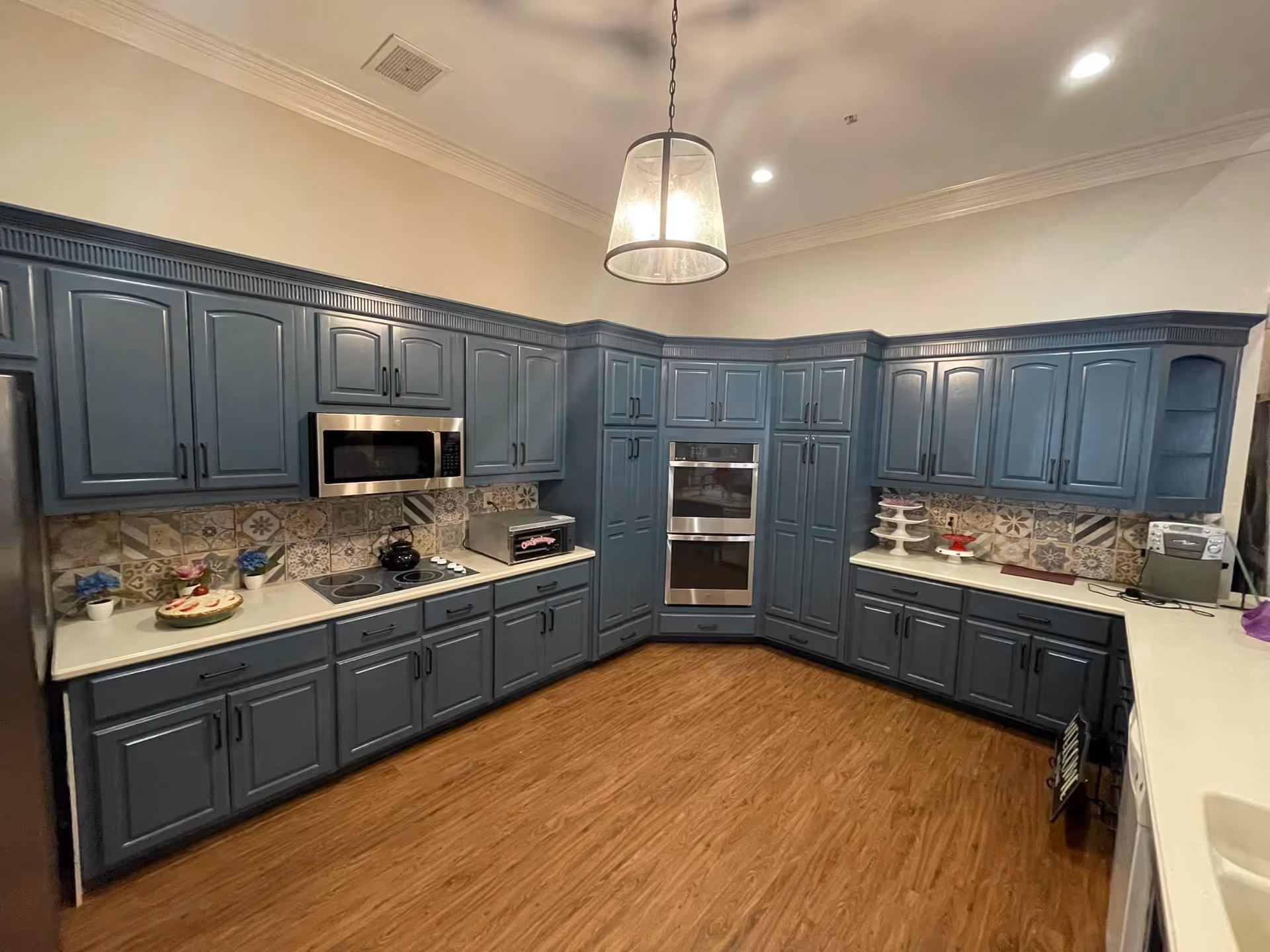 Spacious kitchen with blue cabinets, stainless steel appliances, patterned tile backsplash, and wood flooring.