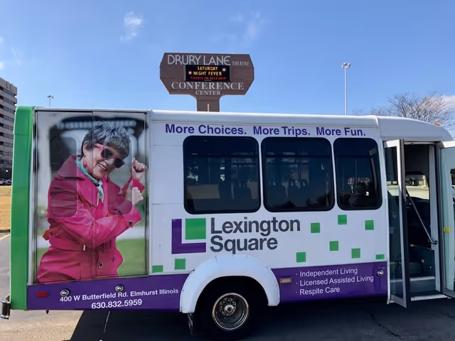 A Lexington Square shuttle bus with purple and green branding parked outside beneath a Drury Lane Conference Center sign.