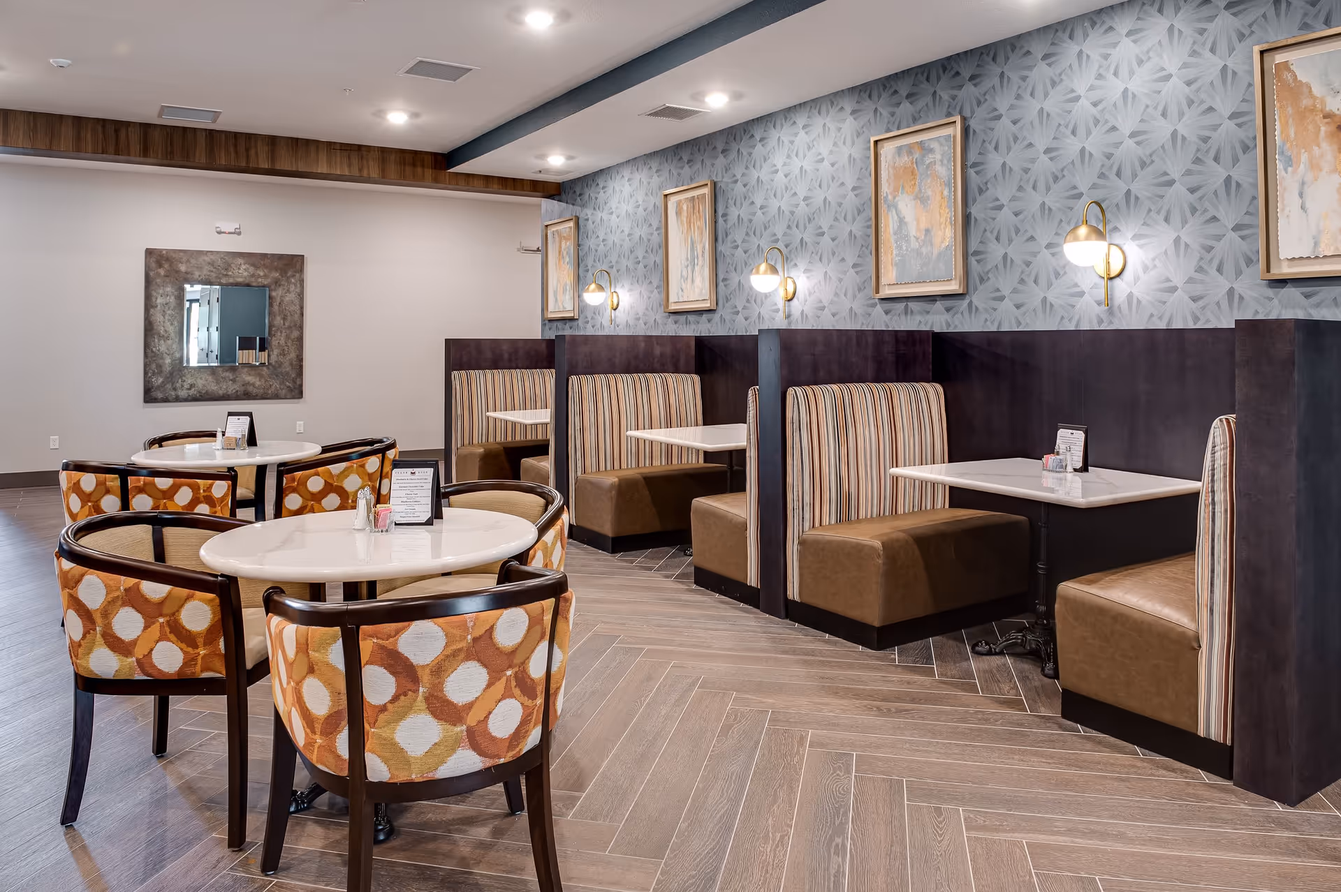 Dining area with round white tables and patterned chairs and leather booths along a patterned accent wall.