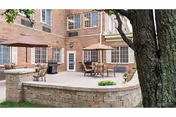 Outdoor patio area with tables, chairs, umbrellas, brick building backdrop, stone planter edge.