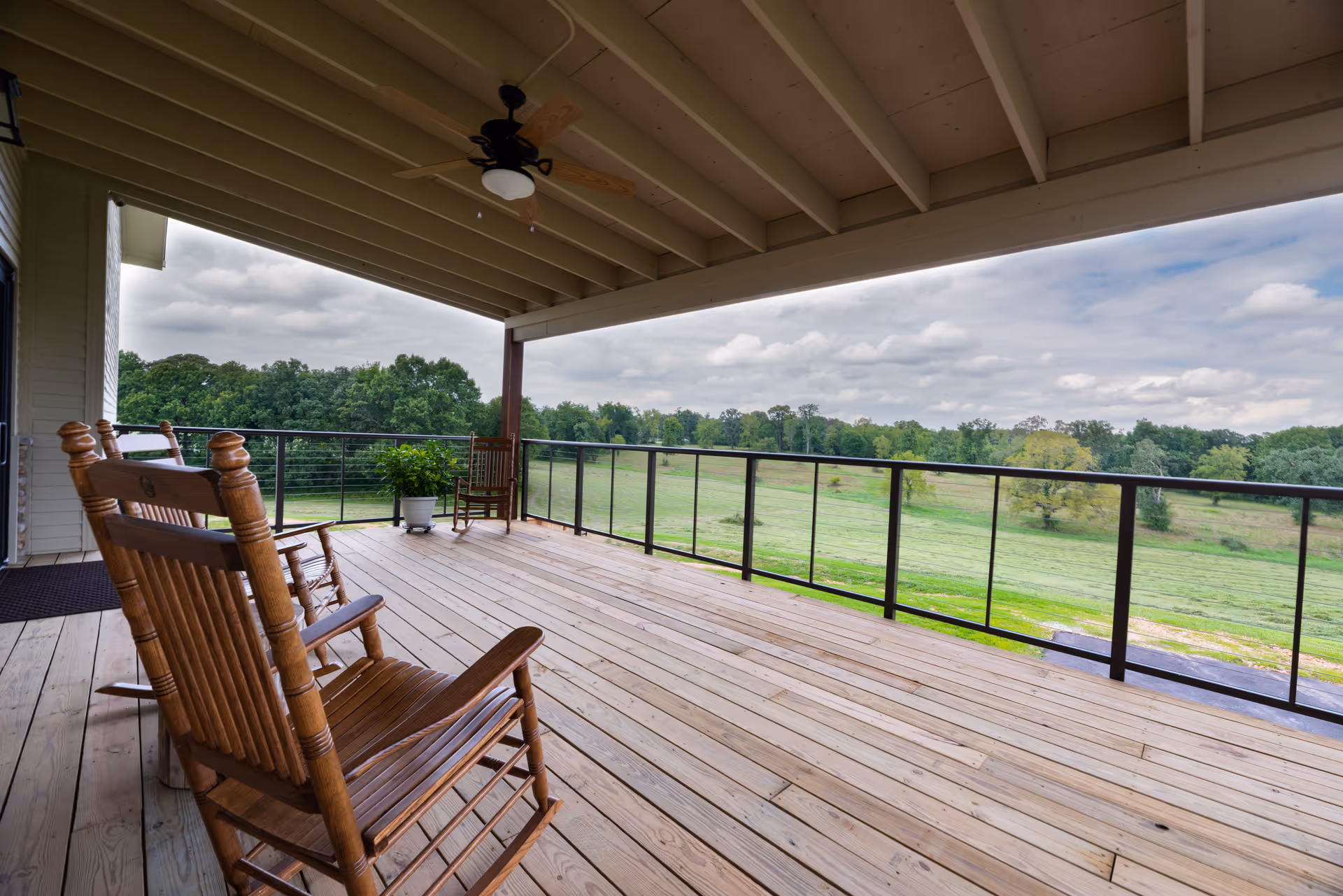 Covered wooden porch with rocking chairs and glass railing overlooking a grassy field.