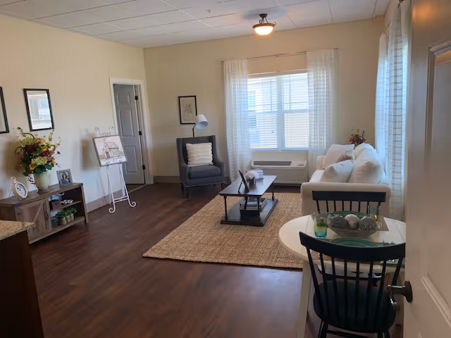 Bright living room with a sofa, armchair, coffee table, small dining table, and a large window.