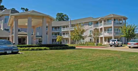 Exterior view of a senior living facility with a covered entrance and parked cars.
