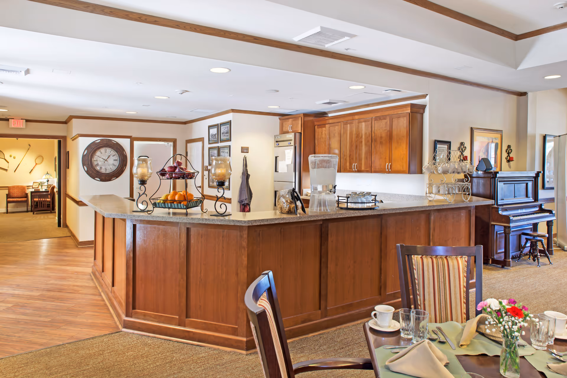 Spacious communal dining area with a wooden service counter and kitchenette, a piano in the corner, and a set dining table in the foreground.