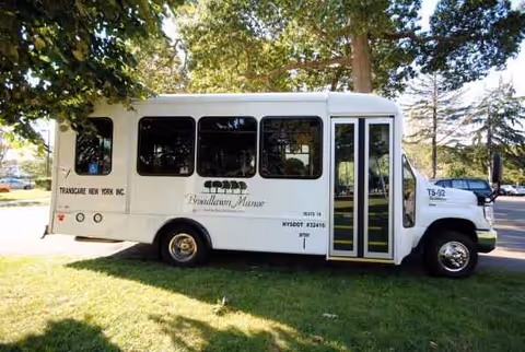 White shuttle bus parked on grass beside trees near a facility.