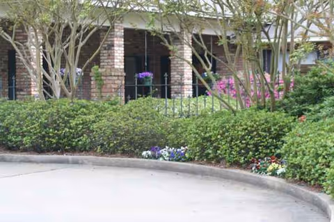 Brick facility entrance with manicured hedges and flowers along the walkway.