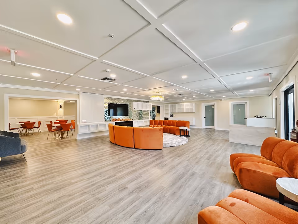 Spacious open interior lounge with curved orange sofas, a TV feature wall, a small dining area, and a reception desk.