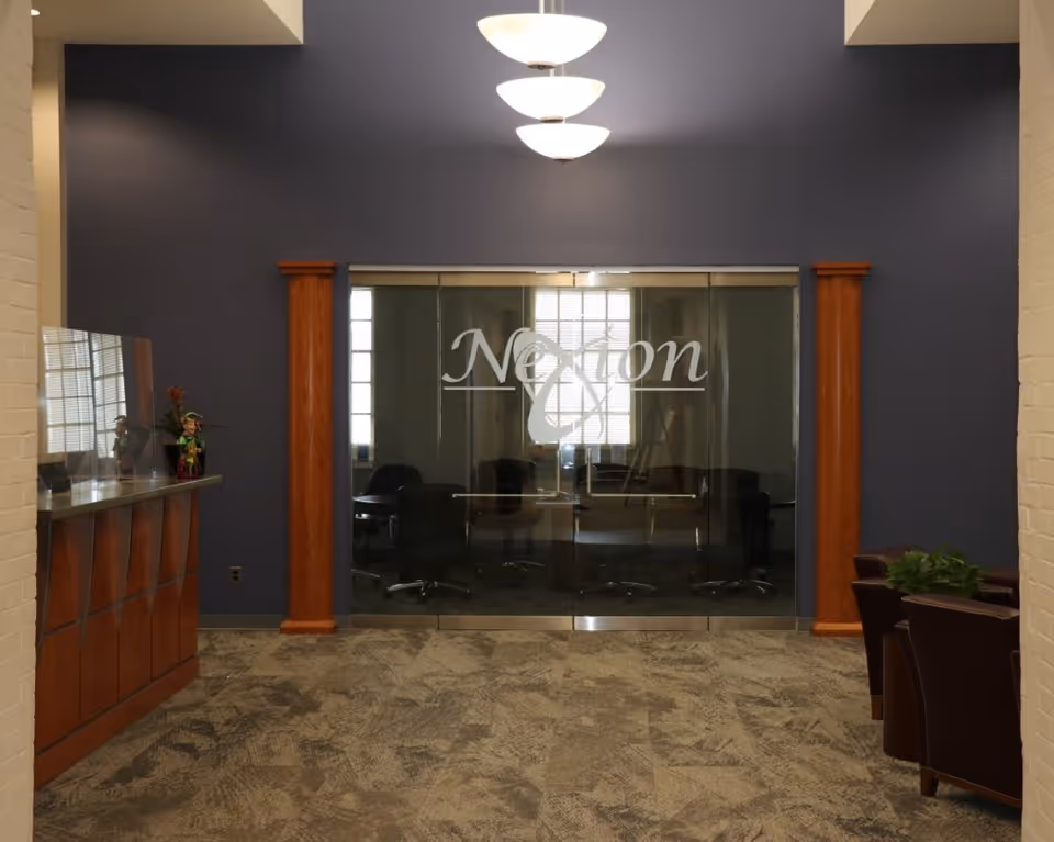 Lobby-style interior with a reception desk, seating, pendant lights, and glass double doors etched with "Nexion".