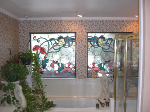 A bathroom with a soaking tub, glass shower, and floral stained-glass windows.