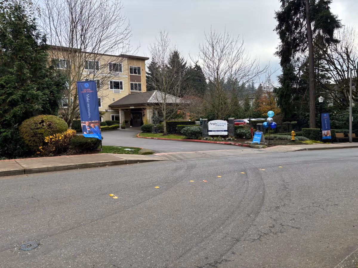 Front entrance of the Aegis Living facility showing the building, driveway, entrance canopy, signage, and balloons.