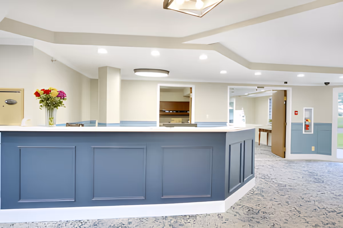 Bright reception desk with a blue paneled front and a vase of flowers in a senior living facility lobby.