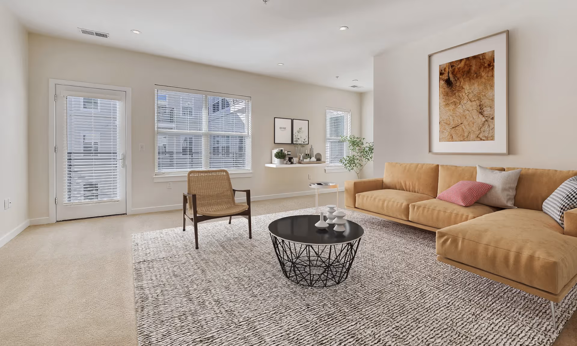 Bright living room with a tan sectional sofa, woven armchair, round black coffee table and large windows.