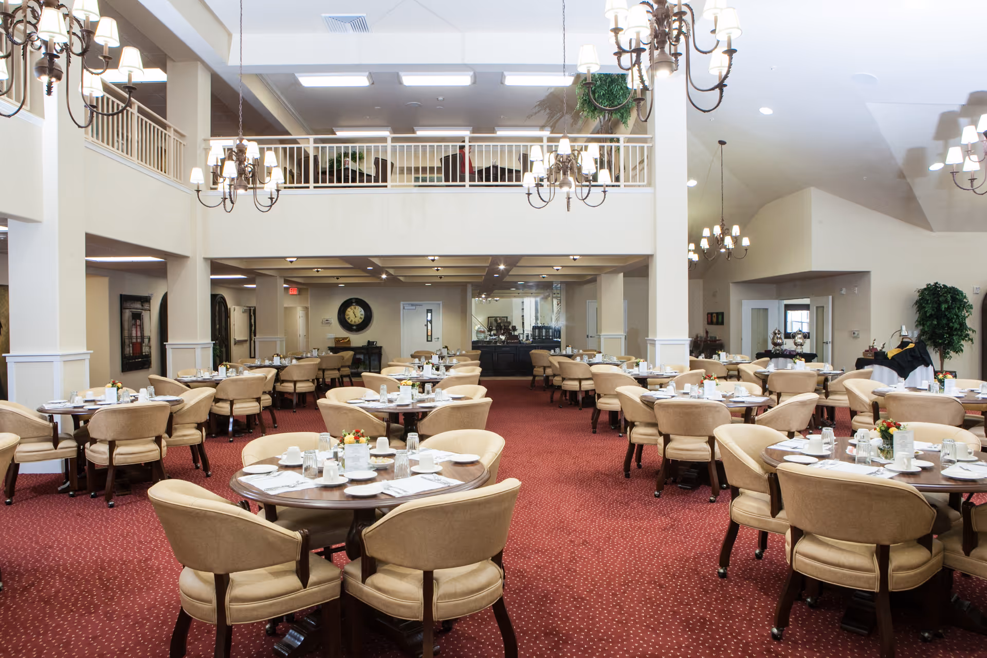 Large elegant dining room with round tables and beige chairs set for meals under chandeliers.