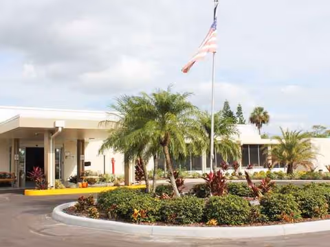 Exterior view of Village Place Health and Rehabilitation Center with palm trees and flag.