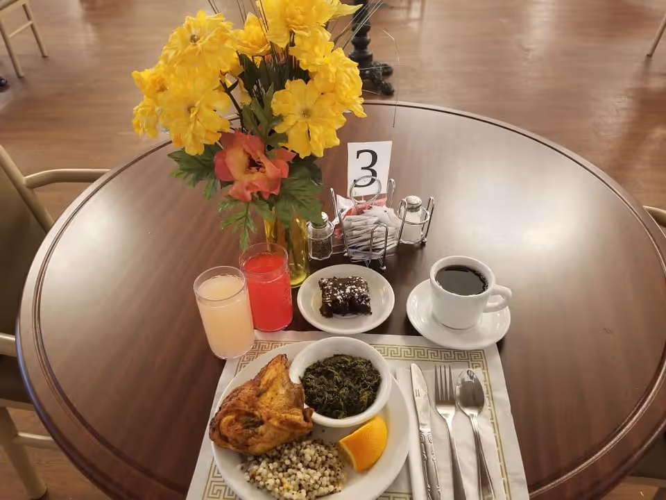 Round dining table set with a plated meal, two drinks, coffee, dessert, silverware and a vase of yellow flowers with table number 3.