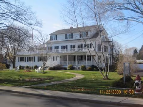 White multi-story senior living building with a front porch, lawn, and curved path.