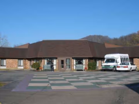 Single-story brick senior living facility exterior with a shuttle bus in the parking area.