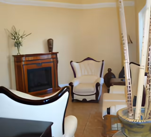 A furnished living room with white upholstered armchairs, a wooden fireplace mantel, and decorative accents.