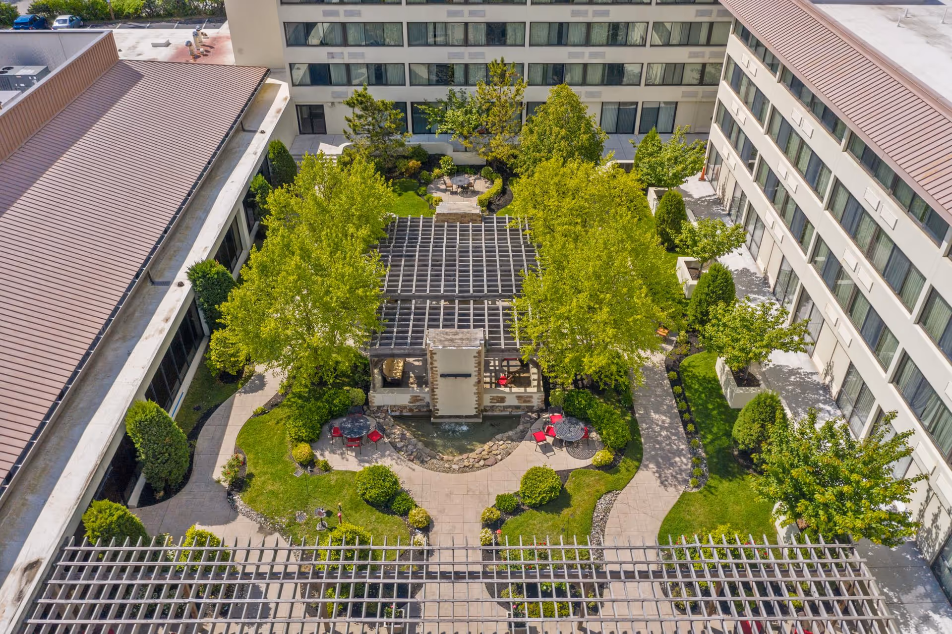Aerial view of a landscaped central courtyard with pergolas, trees, paths, and seating between multi-story buildings.