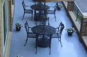 Outdoor covered balcony with wrought-iron tables and chairs and potted plants along the railing.