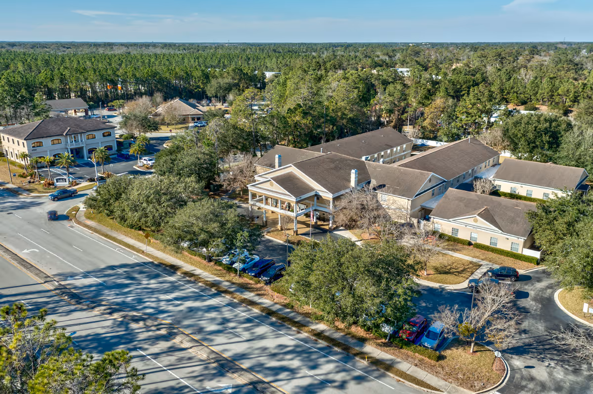 Aerial view of Discovery Commons San Pablo senior living campus with connected beige buildings, a covered main entrance, parking areas, and surrounding trees.