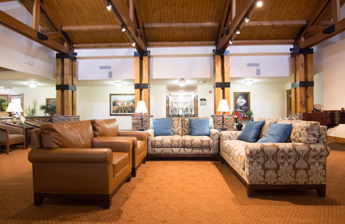 A cozy common lounge with leather armchairs and patterned sofas beneath exposed wooden ceiling beams.