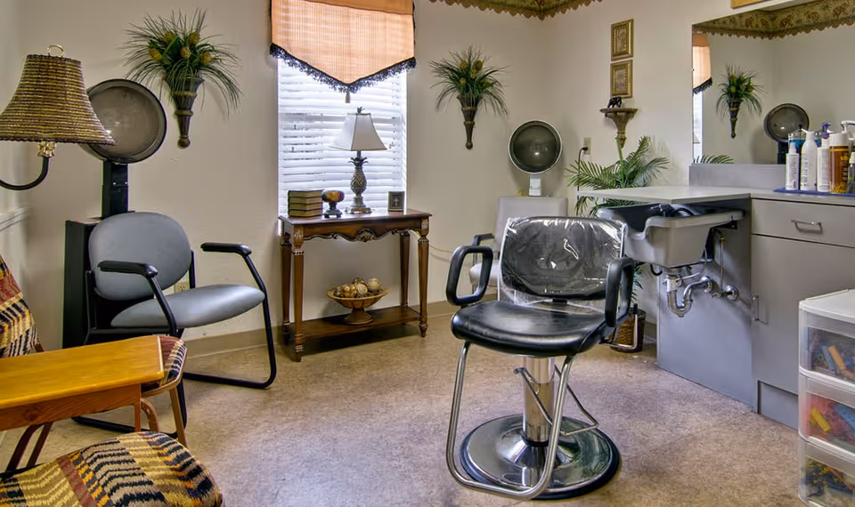 Small hair salon room with a barber chair and styling sink, guest seating, and a decorative table beneath a window.