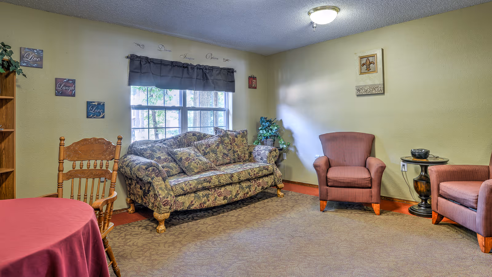 Cozy sitting room with a patterned sofa under a window, two upholstered armchairs, a wooden chair, and a small side table.