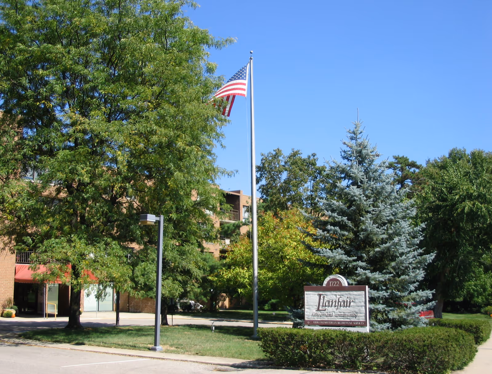 Exterior view of Ohio Living Llanfair retirement community with trees, an American flag on a flagpole, and a sign displaying the community's name and address.
