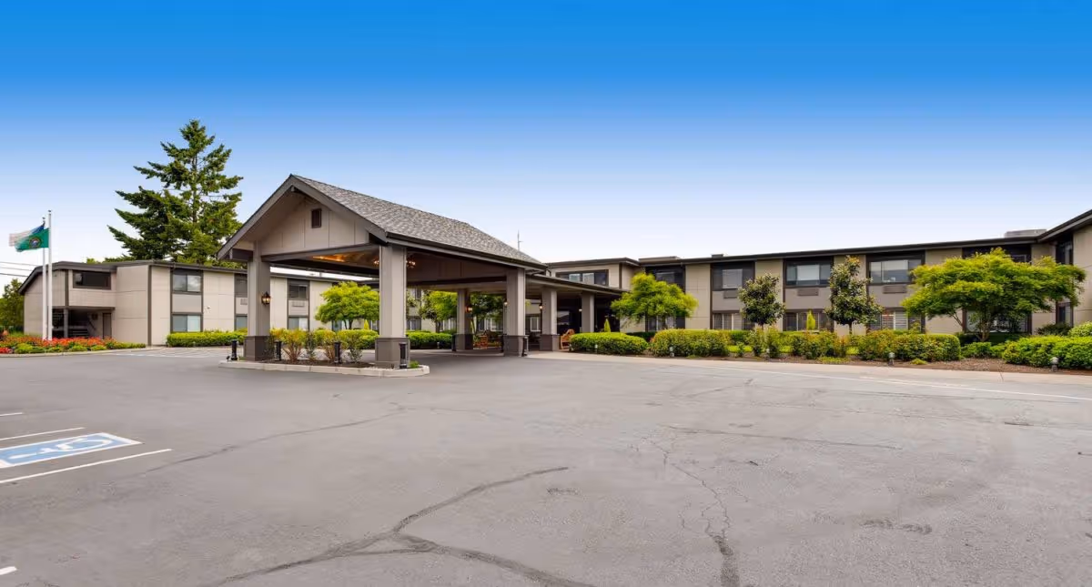 Exterior view of Cascade Inn Assisted Living Community showing a two-story building with a covered entrance, surrounded by well-maintained landscaping and a parking lot with a handicapped parking space.