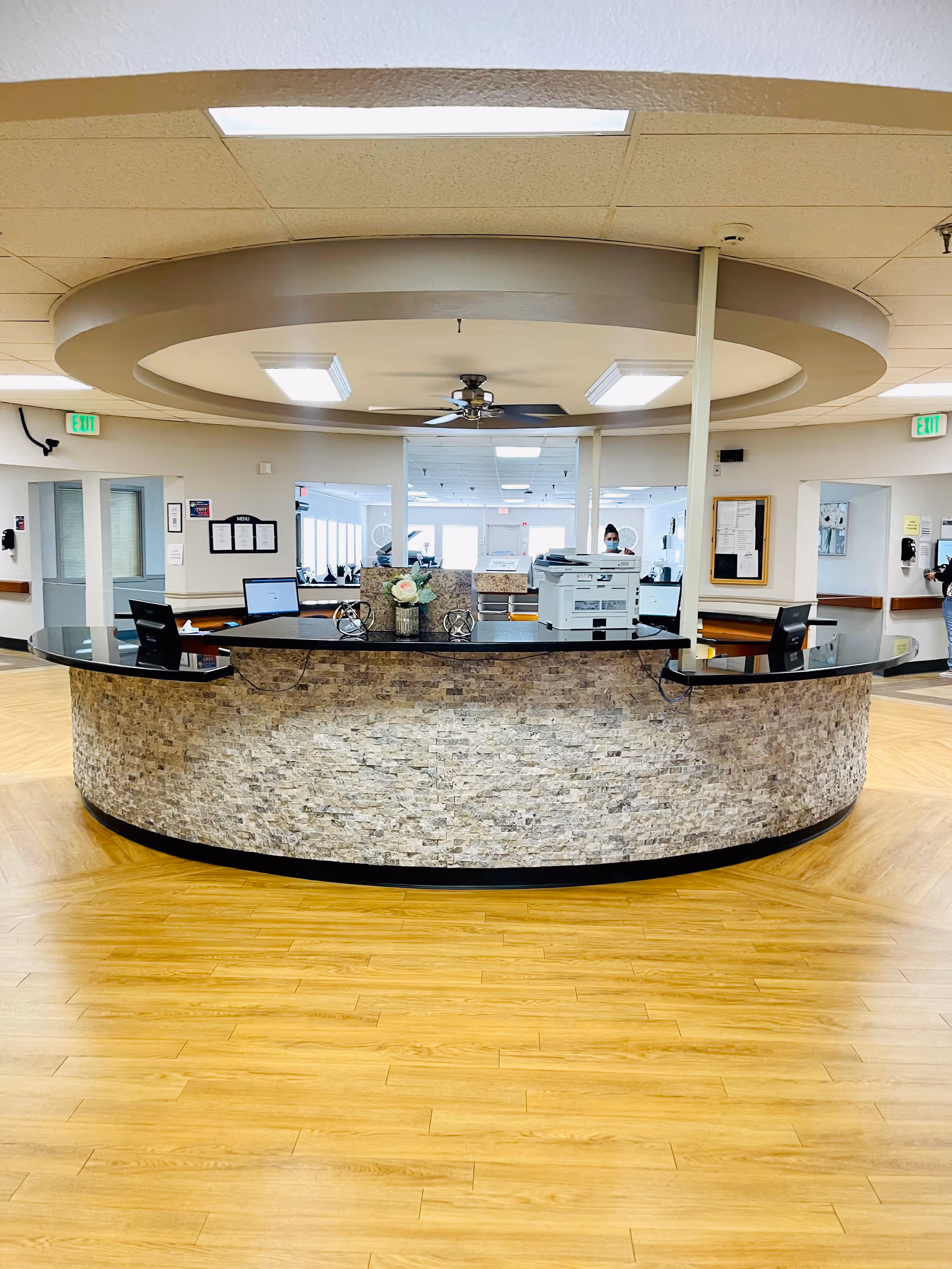 Circular stone-faced reception desk with computers and a decorative ceiling feature in a bright facility lobby.