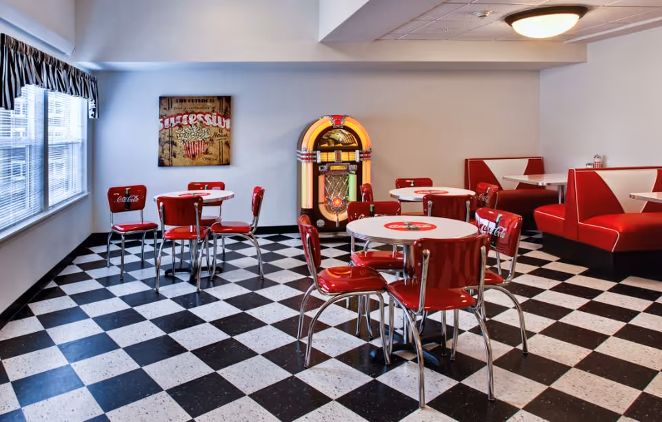 Retro-style dining room with red diner booths and chairs, a jukebox, and a black-and-white checkered floor.