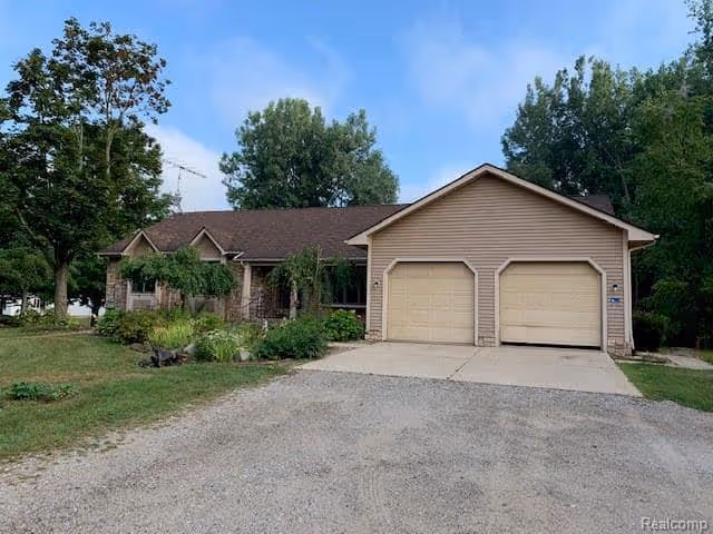Single-story house with a two-car garage, driveway, lawn and trees under a blue sky.