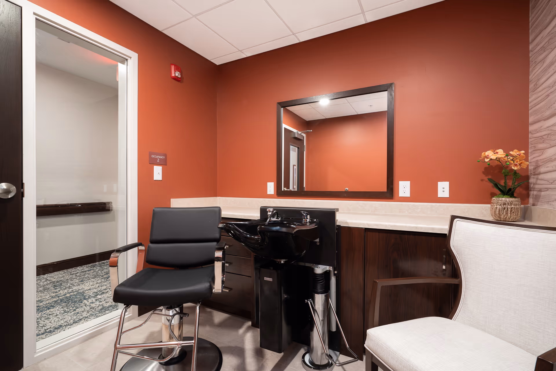 A small salon station with a black styling chair, shampoo sink, mirror and red-painted wall.