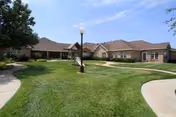 Exterior view of a single-story senior living facility with a green lawn and curved walkway.