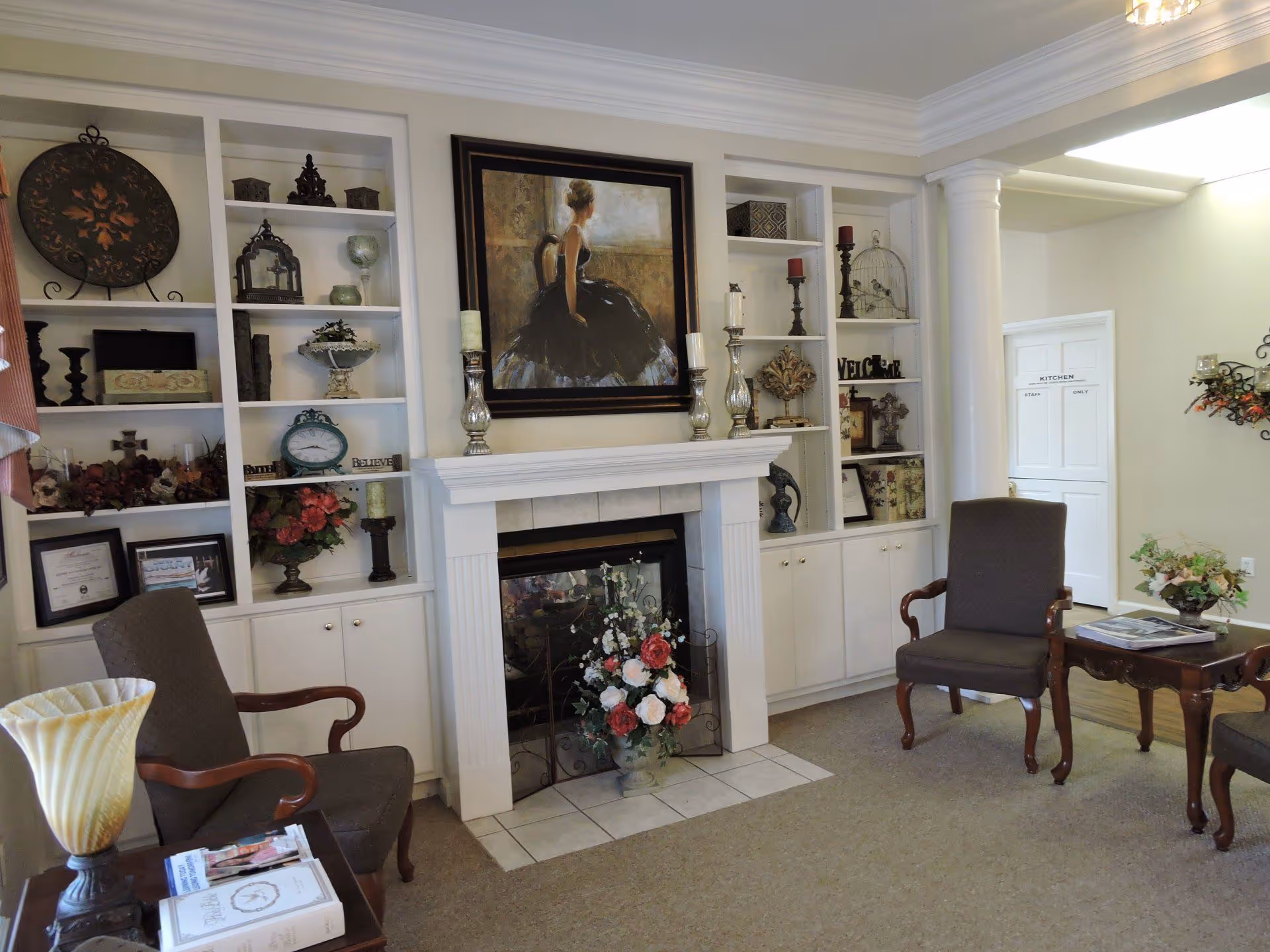A cozy living room with armchairs around a mantel fireplace flanked by built-in shelves filled with decorative items.