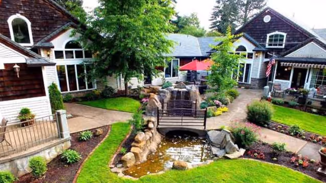 An outdoor courtyard between RiverCrest Senior Living buildings featuring a small bridge, pond, and landscaped pathways.