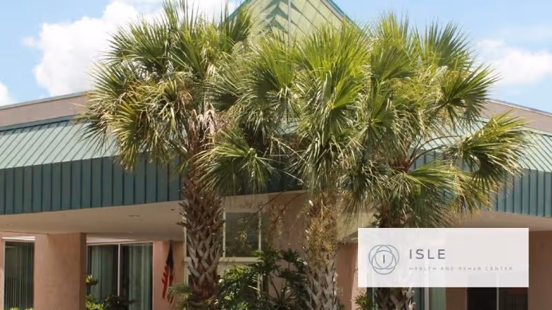 Front entrance of a green-roofed building framed by palm trees with an 'Isle Health and Rehab Center' logo watermark.