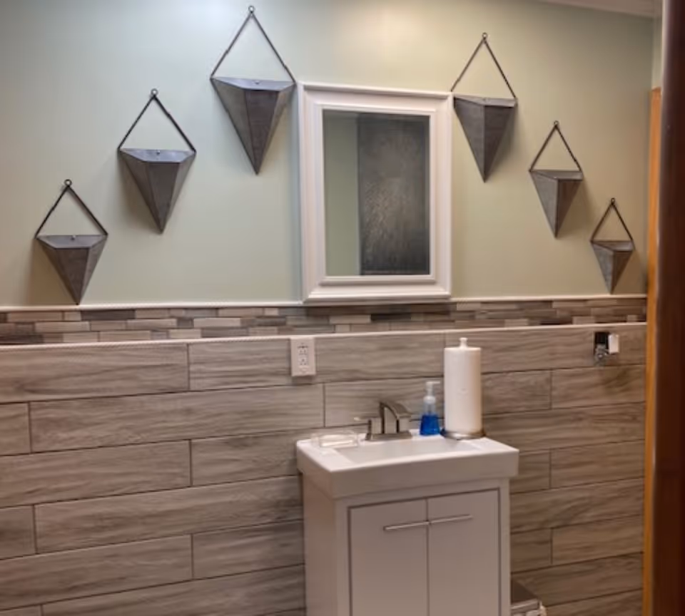 Small bathroom with a vanity sink and mirror, tiled wainscoting, and decorative hanging metal planters on a light green wall.