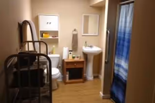 Compact beige bathroom with pedestal sink, toilet, wall cabinet, mirror, and blue striped shower curtain.