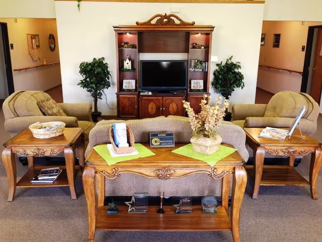Seating area with a sofa and two armchairs facing a wooden entertainment center with a TV, flanked by side tables and potted plants.
