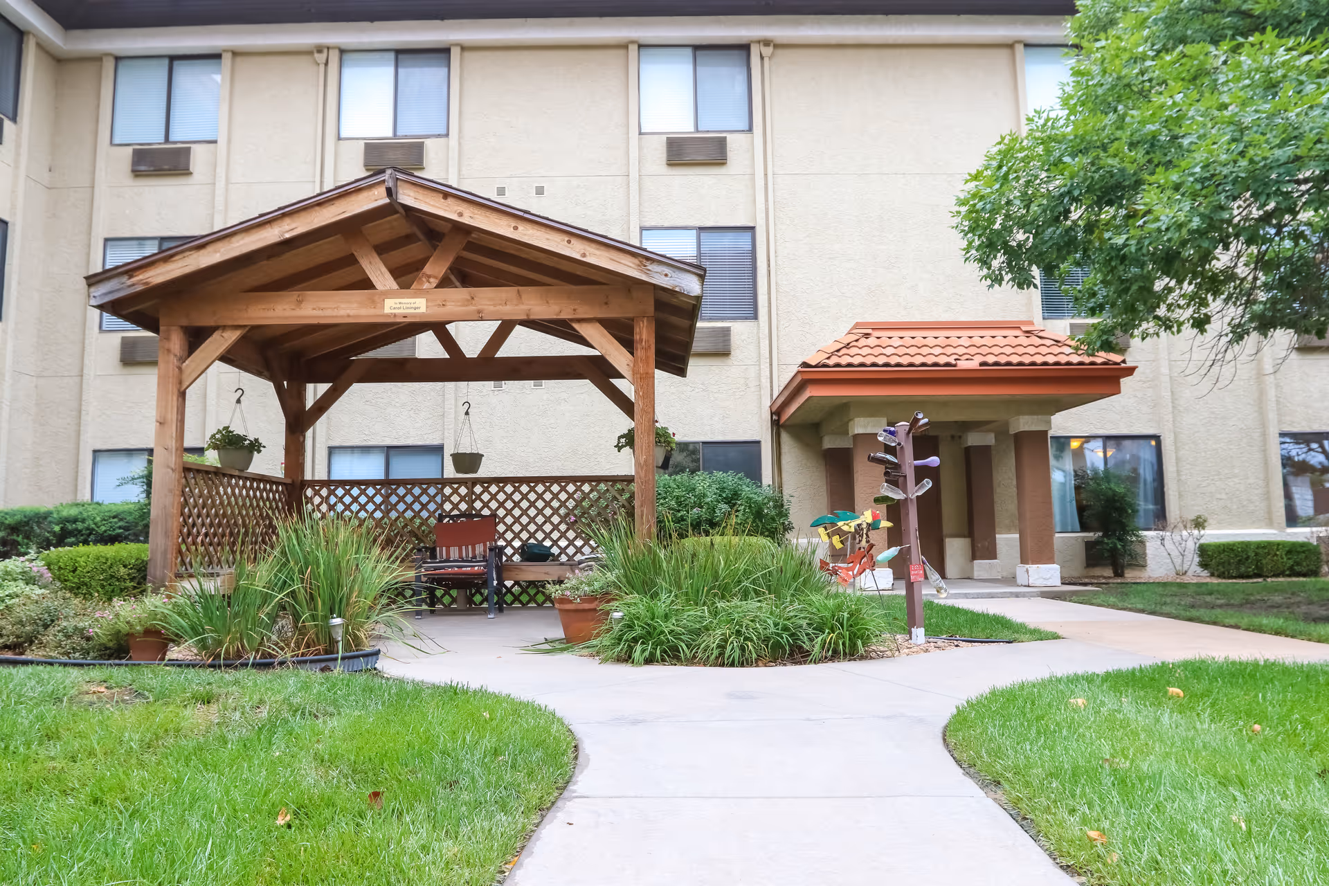 Wooden gazebo and landscaped walkway leading to the entrance of a multi-story senior living building.