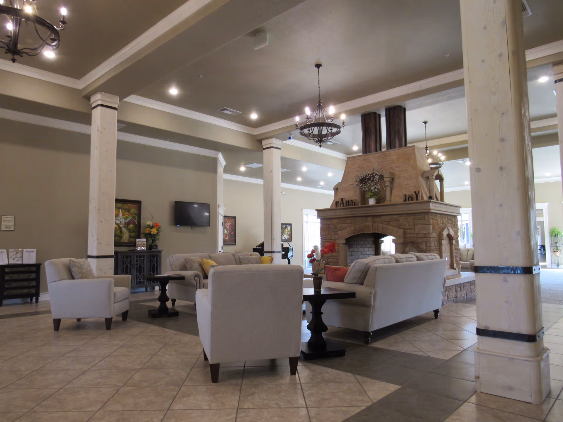 Spacious lounge with beige sofas, columns, chandeliers, and a central stone fireplace.