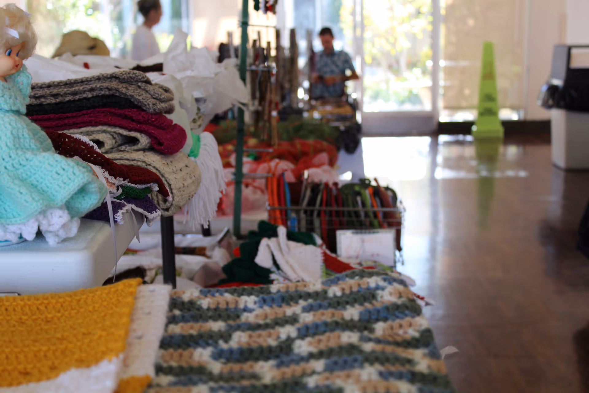 Tables displaying folded knitted and crocheted blankets and crafts in a bright interior room.
